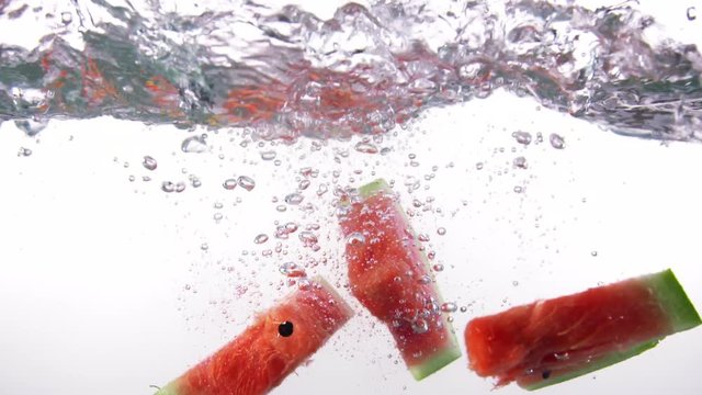 Fresh ripe watermelon slices falls into water with splashes on white background slow motion close-up