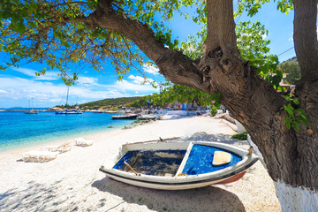 Sunny summer beach in Greece with sun beds and small boat