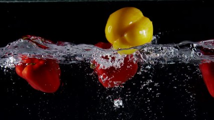 Slow motion of fresh vegetables sweet yellow red bell peppers falling into clear water with splashes on black background - Powered by Adobe