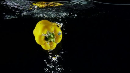Slow motion of yellow bell pepper falling into clear water with splashes on black background - Powered by Adobe