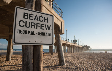 Beach curfew times on sign under the pier of Huntington beach in Southern California