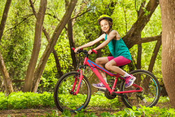 Naklejka premium Smiling young girl cycling through spring woodland