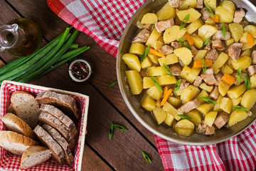 Stewed potatoes with meat in a frying pan on a wooden table. Top view