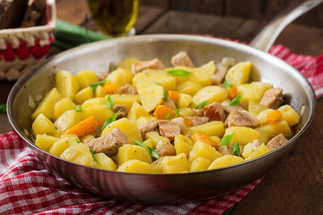 Stewed potatoes with meat in a frying pan on a wooden table
