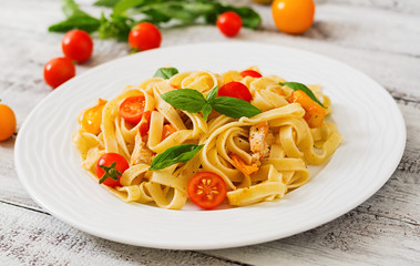 Fettuccine pasta in tomato sauce with chicken, tomatoes decorated with basil on a wooden table