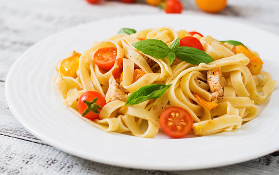 Fettuccine pasta in tomato sauce with chicken, tomatoes decorated with basil on a wooden table