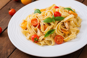 Fettuccine pasta in tomato sauce with chicken, tomatoes decorated with basil on a wooden table