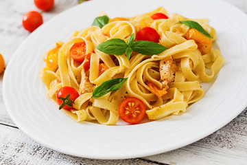 Fettuccine pasta in tomato sauce with chicken, tomatoes decorated with basil on a wooden table