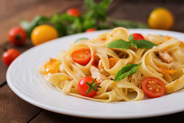 Fettuccine pasta in tomato sauce with chicken, tomatoes decorated with basil on a wooden table