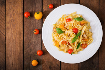 Fettuccine pasta in tomato sauce with chicken, tomatoes decorated with basil on a wooden table. Top...