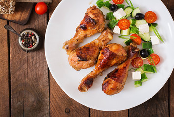 Appetizing oven baked golden chicken drumsticks and Greek salad. Top view