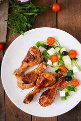 Appetizing oven baked golden chicken drumsticks and Greek salad. Top view