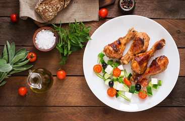 Appetizing oven baked golden chicken drumsticks and Greek salad. Top view