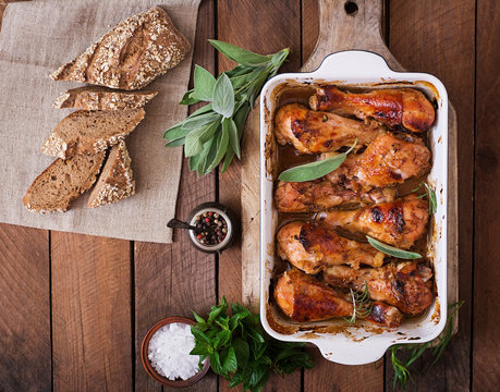 Appetizing oven baked golden chicken drumsticks in a baking dish on a wooden table. Top view