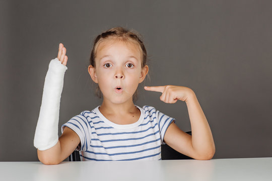 Young surprised girl with broken arm is sitting at the table. 