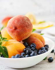 Fresh peaches and blueberries in bowl on a light wooden background in rustic style