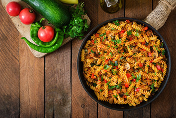 Vegetarian Vegetable pasta Fusilli with zucchini, mushrooms and capers in pan on wooden table. Top view