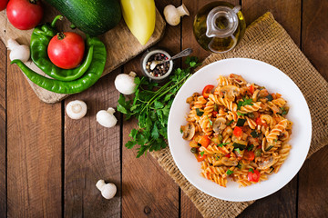 Vegetarian Vegetable pasta Fusilli with zucchini, mushrooms and capers in white bowl on wooden...