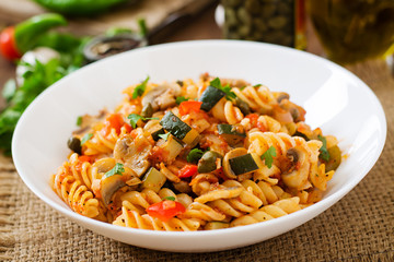 Vegetarian Vegetable pasta Fusilli with zucchini, mushrooms and capers in white bowl on wooden table