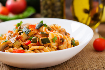 Vegetarian Vegetable pasta Fusilli with zucchini, mushrooms and capers in white bowl on wooden table