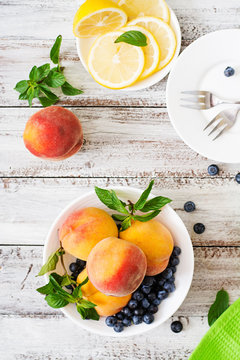 Fresh peaches and blueberries in bowl on a light wooden background in rustic style. Top view