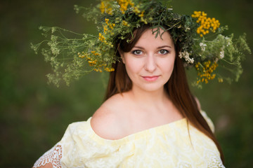 young beautiful woman in wreath of flowers outdoors in nature


