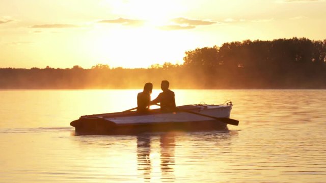 Romantic golden river sunset. Loving couple on small boat backlit by sunlight