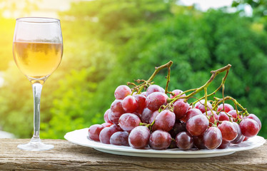 White wine in glass and purple grapes in a dish on the wood floor with the green nature and sunlight background.