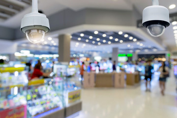 Closeup CCTV security camera on blurred inside shopping mall background.
