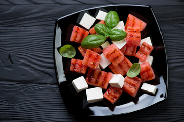 Salad with grilled watermelon and feta on a black wooden surface