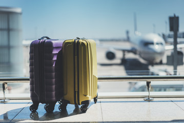 Two suitcases in the airport departure lounge, airplane in the blurred background, summer vacation concept, traveler suitcases in airport terminal waiting area - obrazy, fototapety, plakaty