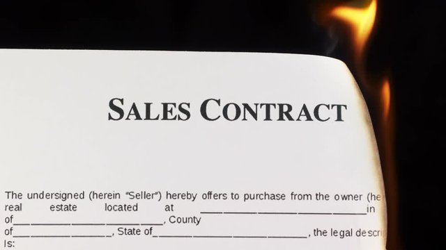 Closeup of white sheet of paper with text sales contract burning in fire on a black background