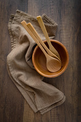 Rustic kitchenware background. A wooden bowl with spoon, fork and a brown napkin on wooden table