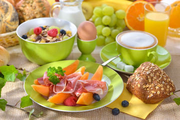 Reichlich gedeckter Fr&uuml;hst&uuml;ckstisch mit Schinken und Melone - Laid breakfast table with melon and ham against a white background