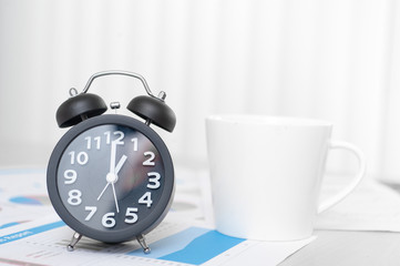 Black alarm clock and coffee place on wood table