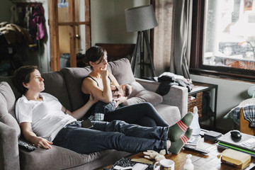 Two women, a couple at home, sitting on the sofa, one breastfeeding a baby. 