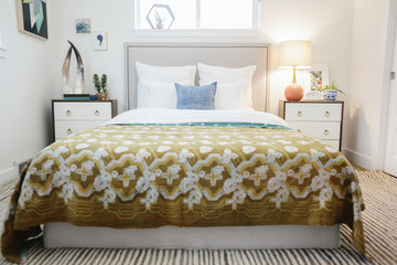 A bedroom in an apartment with a double bed covered with a patterned retro look bedspread.