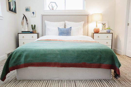 A green fabric quilt with red trim over a double bed in a light airy apartment.