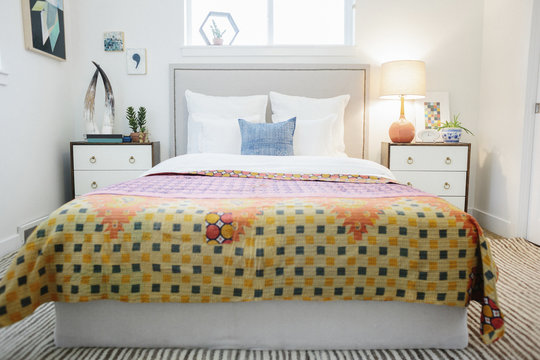 A bedroom in an apartment with a double bed and beside cabinets, and a vivid patched patterned bedspread in orange and yellow.