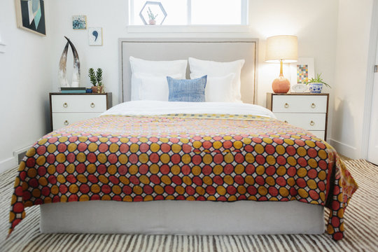 A bedroom in an apartment with a double bed and beside cabinets, and a vivid retro style patterned bed cover.
