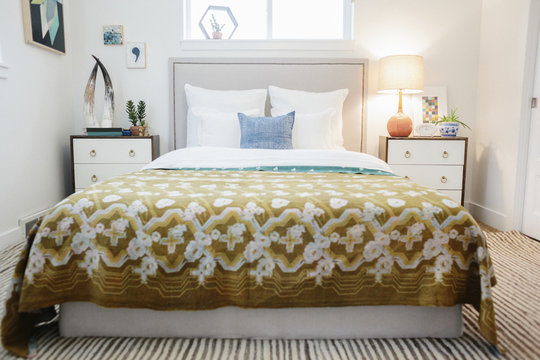 A bedroom in an apartment with a double bed covered with a patterned retro look bedspread.