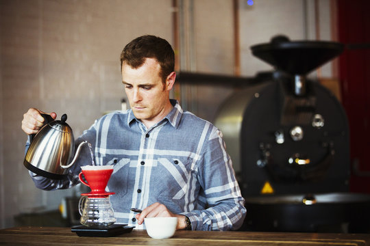 Specialist coffee shop. A man brewing coffee using a filter paper, and drinking it. 