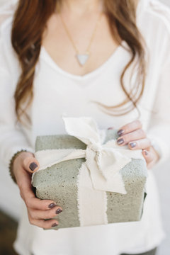 A woman holding a gift wrapped box with a broad ribbon tied in a bow. 