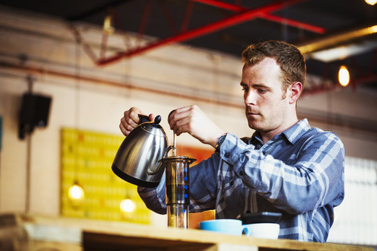 Specialist coffee shop. A man pouring hot water into a coffee percolator.