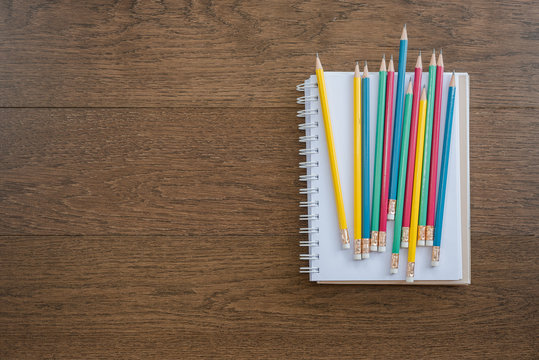 multicolor pencils and blank notebook on wooden background