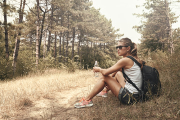 Female trekker resting on the ground with water bottle. Young active woman hiking on the nature.