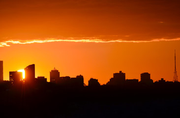 Fototapeta na wymiar Glowing orange sun setting behind city buildings in silhouette (North Sydney, Australia)