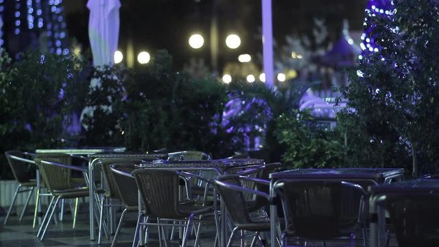 Empty terrace bar at night with Christmas street lights and people walking in the background, static shot