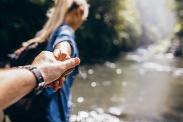 Two hikers in nature crossing the stream holding hands © Jacob Lund