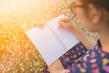 woman writing in her diary on the meadow with white flowers